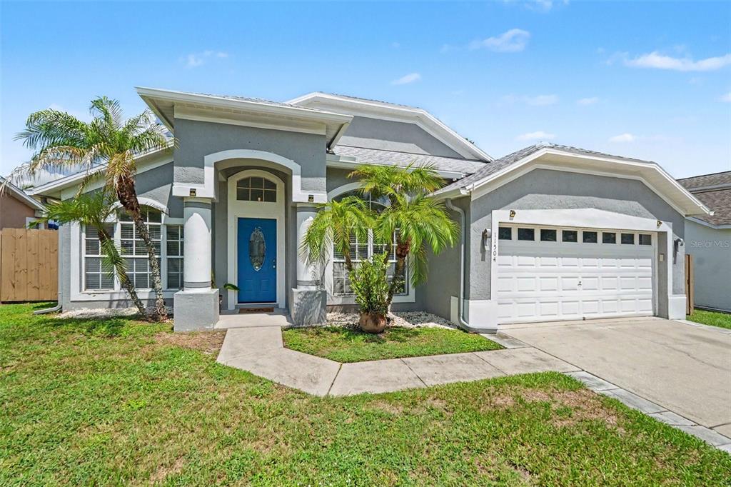 A single-story gray house with a blue front door, a two-car garage, and palm trees — 11504 WELLMAN DRIVE, RIVERVIEW, FL