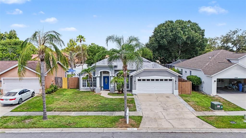 A single-story suburban house with a gray exterior, blue front door, and a two-car garage — 11504 WELLMAN DRIVE, RIVERVIEW, FL