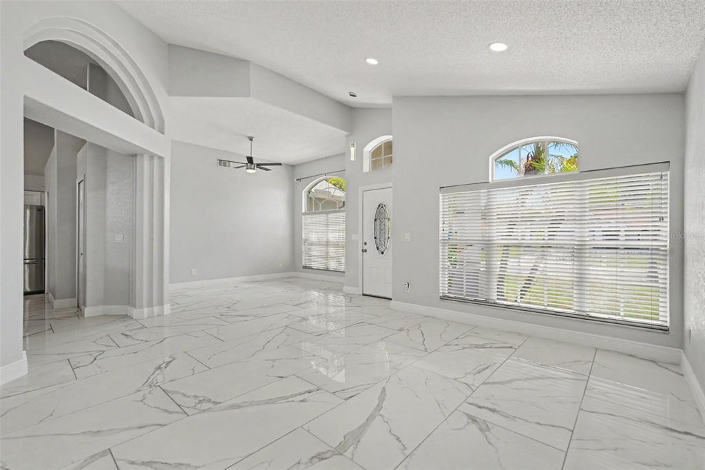 A bright living room features white marble-look tile floors, vaulted ceilings, and large arched windows — 11504 WELLMAN DRIVE, RIVERVIEW, FL
