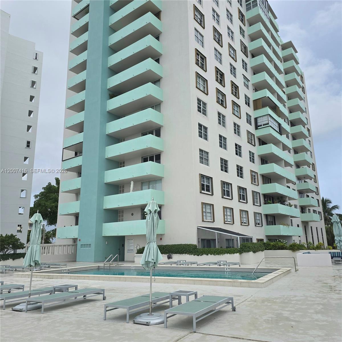 A tall residential building with turquoise balconies overlooks a swimming pool and lounge chairs — 5 Island Ave # 5A, Miami Beach FL 33139, MIAMI BEACH, FL