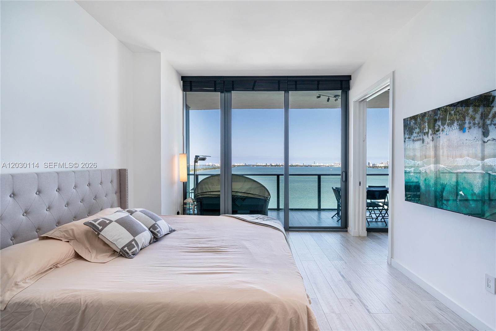 A bedroom with a tufted headboard, light wood floors, and a balcony overlooking the water — 480 NE 31st St # 1603, Miami FL 33137, MIAMI, FL