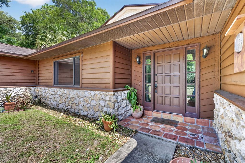 A brown wooden front door with side windows sits under an overhang on a stone-faced house — 551 RYLANE STREET, DE LEON SPRINGS, FL