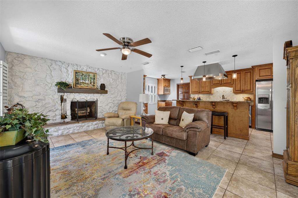 A living room with a stone fireplace, brown sofa, and an open kitchen with wooden cabinets — 551 RYLANE STREET, DE LEON SPRINGS, FL