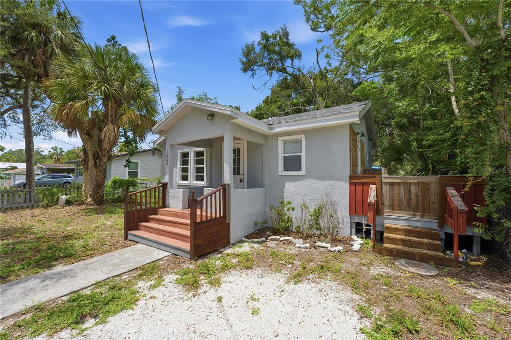 A small, light gray house with a front porch, wooden steps, and a gravel driveway — 1553 29TH STREET, SARASOTA, FL