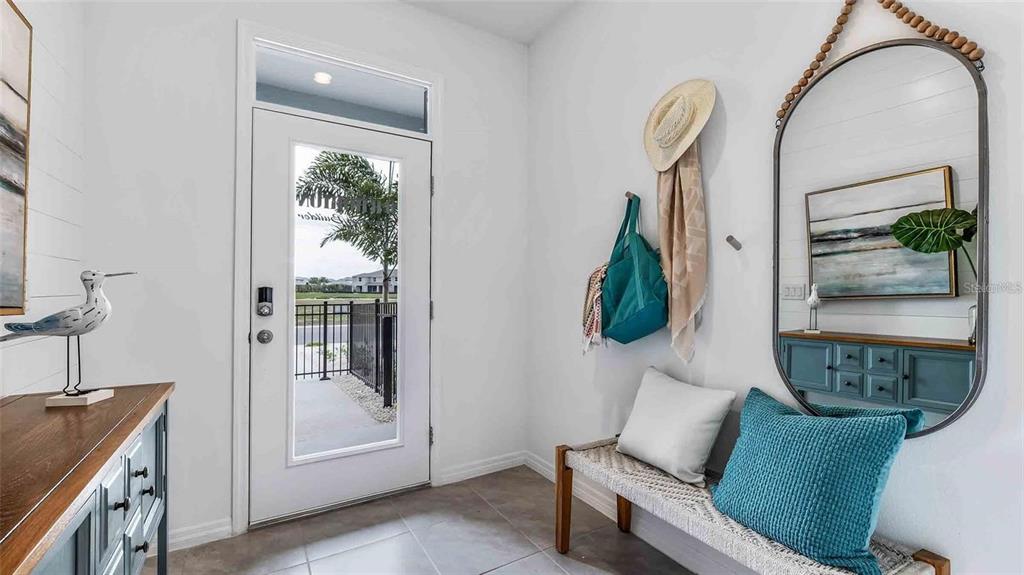 An entryway features a white door, a bench with pillows, a mirror, and a console table — 32311 TURTLE GRACE LOOP, WESLEY CHAPEL, FL