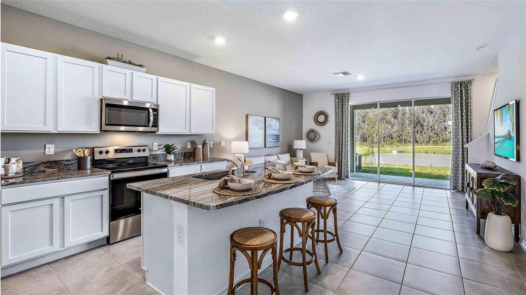 A kitchen with white cabinets and granite countertops opens to a living area with tile — 32311 TURTLE GRACE LOOP, WESLEY CHAPEL, FL