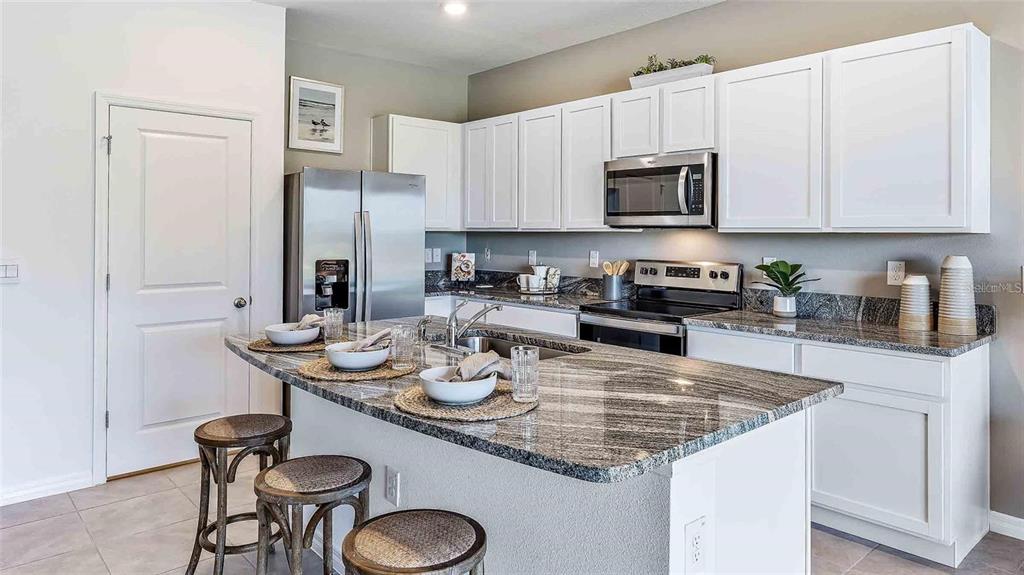 A kitchen features white cabinets, granite countertops, stainless steel appliances, and a breakfast bar island — 32311 TURTLE GRACE LOOP, WESLEY CHAPEL, FL