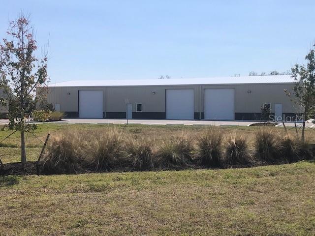 A single-story commercial metal building with three large roll-up doors and a paved parking lot — 134 ANCHOR ROAD UNIT 203, ROTONDA WEST, FL