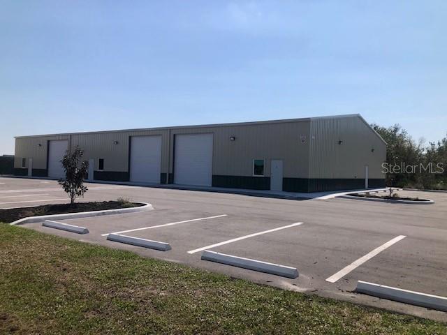 A long, metal-sided commercial warehouse building features multiple roll-up doors and a paved parking lot — 134 ANCHOR ROAD UNIT 203, ROTONDA WEST, FL