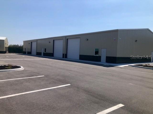 A large, beige metal industrial building with multiple roll-up doors sits in a paved parking lot — 134 ANCHOR ROAD UNIT 203, ROTONDA WEST, FL