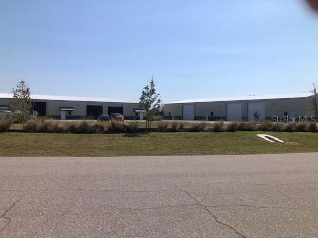Two large, light-colored industrial warehouse buildings stand behind a grassy lot and paved road — 134 ANCHOR ROAD UNIT 203, ROTONDA WEST, FL