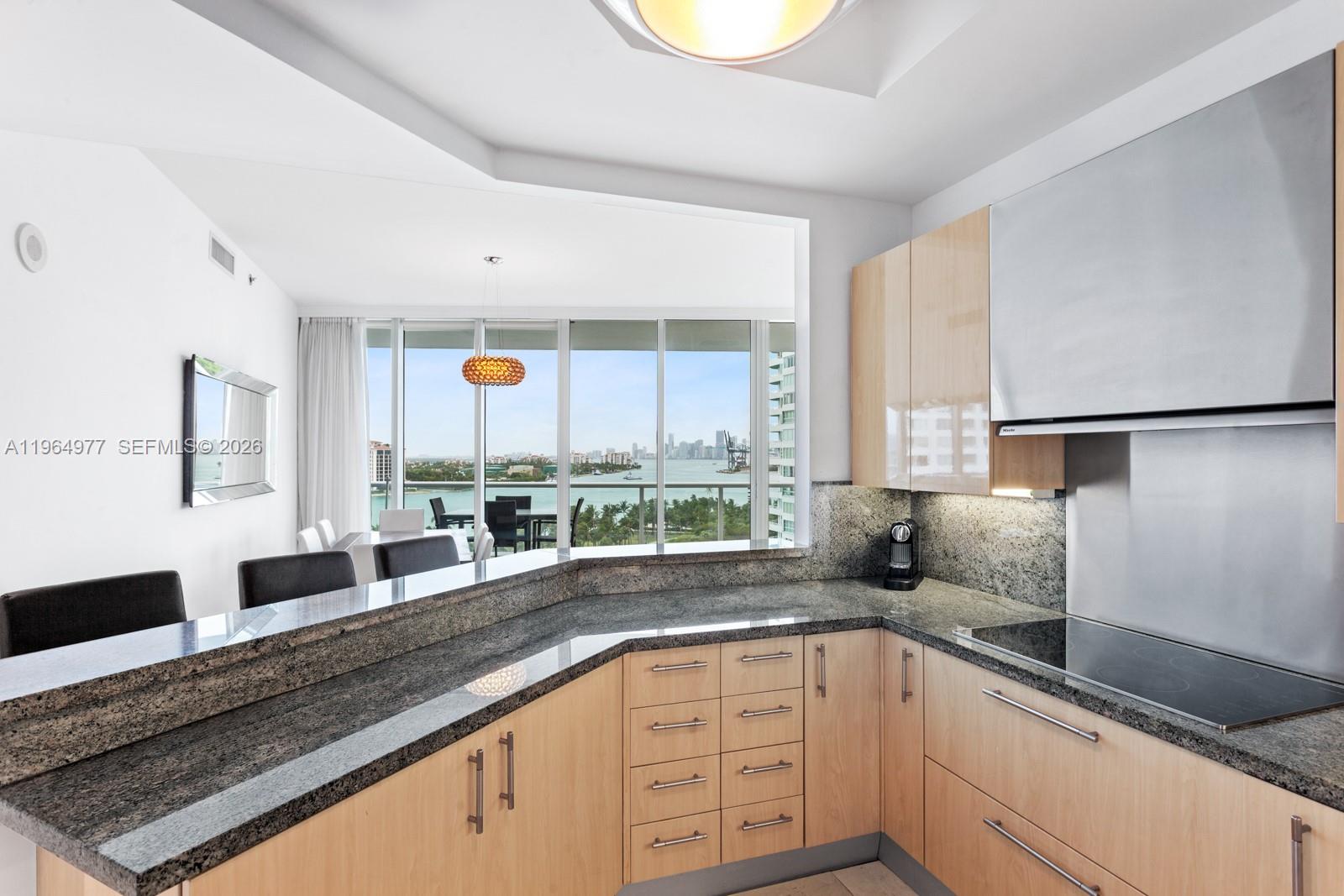 A kitchen with light wood cabinets, granite countertops, and a view of the city skyline — 100 S Pointe Dr # 1001, Miami Beach FL 33139, MIAMI BEACH, FL