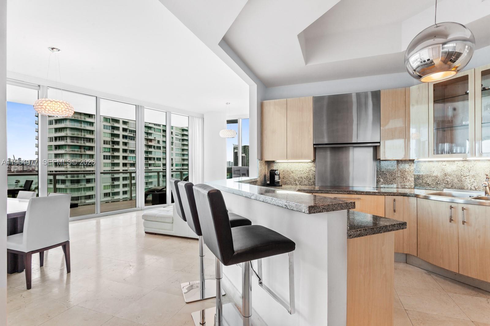 A modern kitchen features light wood cabinets, granite countertops, and a breakfast bar with stools — 100 S Pointe Dr # 1001, Miami Beach FL 33139, MIAMI BEACH, FL