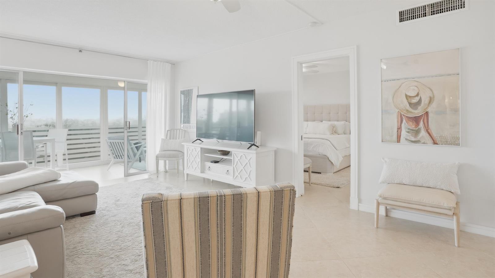 A bright living room features white tile floors, a television console, and a balcony view — 921 Spanish Circle # 436, Delray Beach FL 33483, DELRAY BEACH, FL
