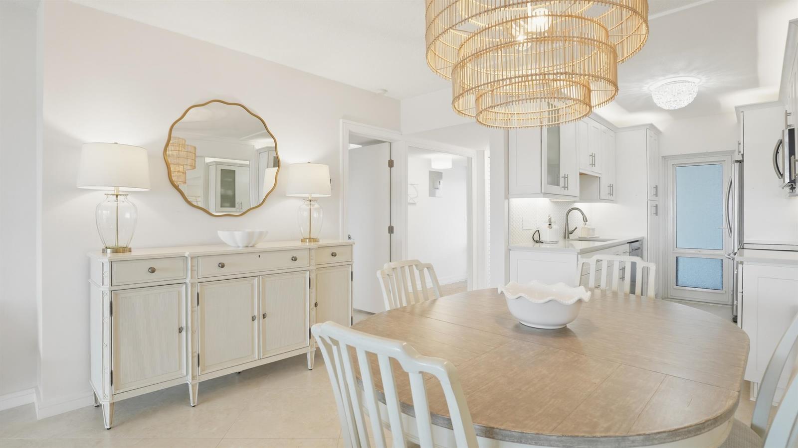 A dining room with a wooden table, white buffet, round mirror, and large rattan chandelier — 921 Spanish Circle # 436, Delray Beach FL 33483, DELRAY BEACH, FL
