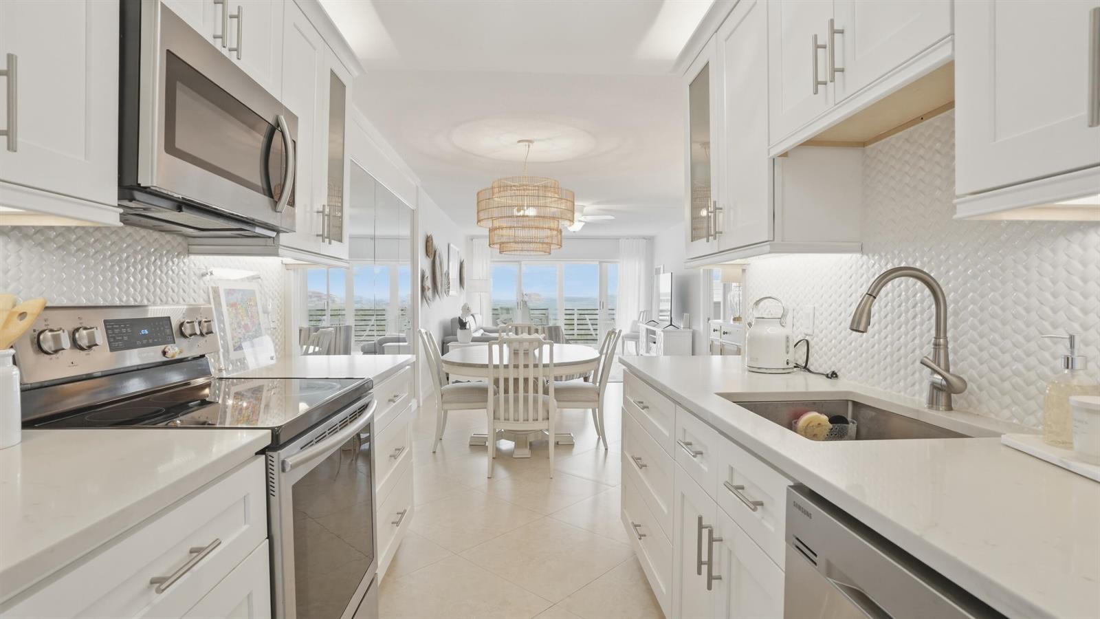 A bright white kitchen with stainless steel appliances leads to a dining area and ocean view — 921 Spanish Circle # 436, Delray Beach FL 33483, DELRAY BEACH, FL