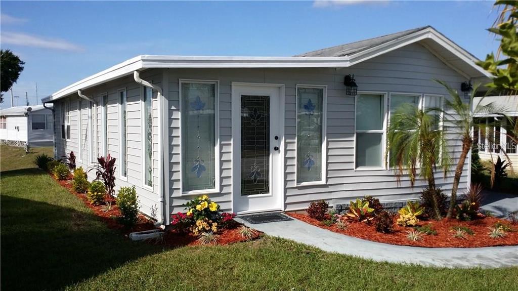 A light gray mobile home features a white front door and surrounding landscaping — 50989 HIGHWAY 27 UNIT 79, DAVENPORT, FL