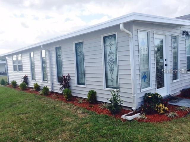 The exterior of a light gray mobile home features decorative glass windows and red mulch landscaping — 50989 HIGHWAY 27 UNIT 79, DAVENPORT, FL