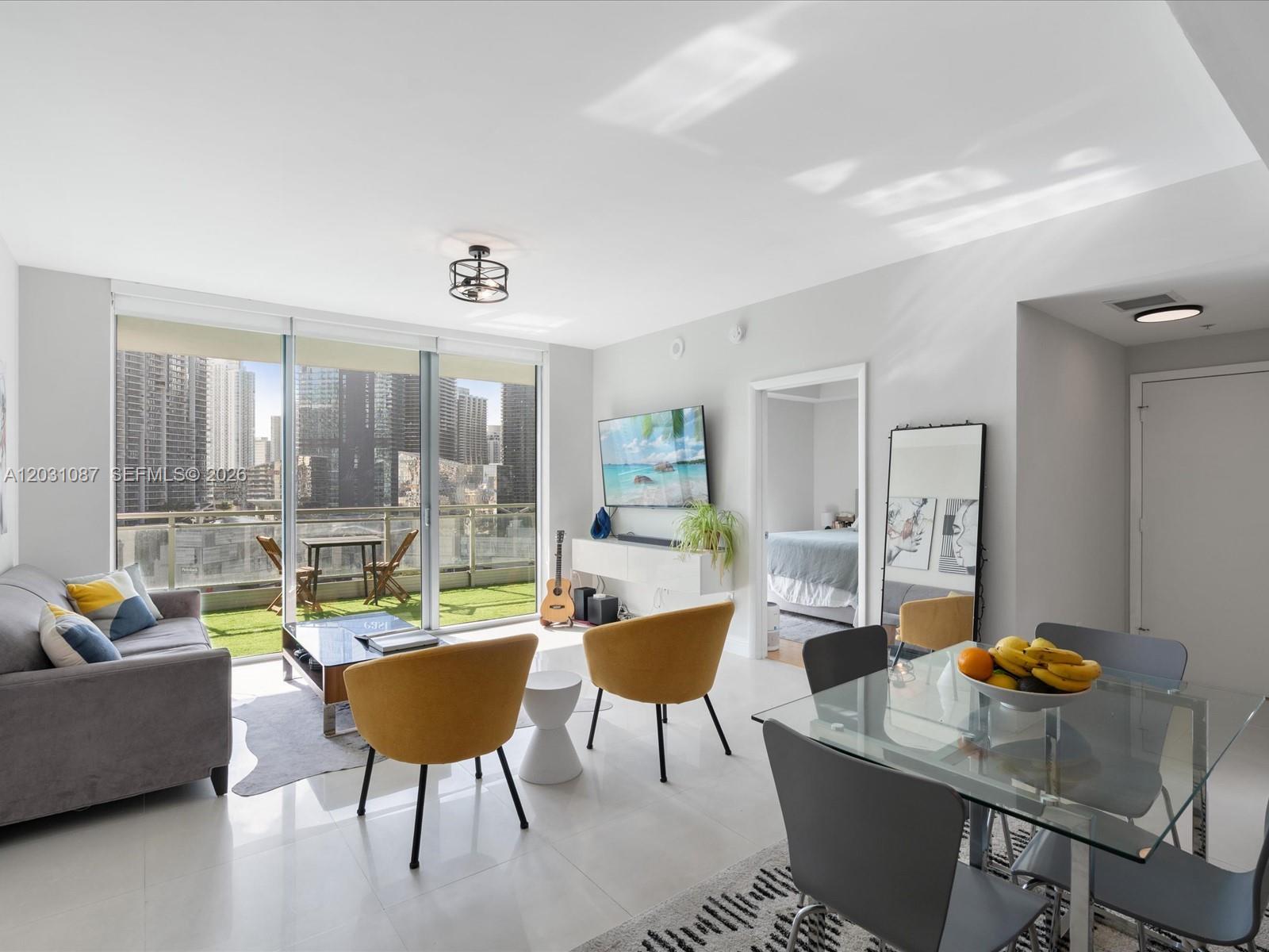A bright living and dining area features white tile floors, yellow chairs, and a balcony — 90 SW 3rd St # 2015, Miami FL 33130, MIAMI, FL