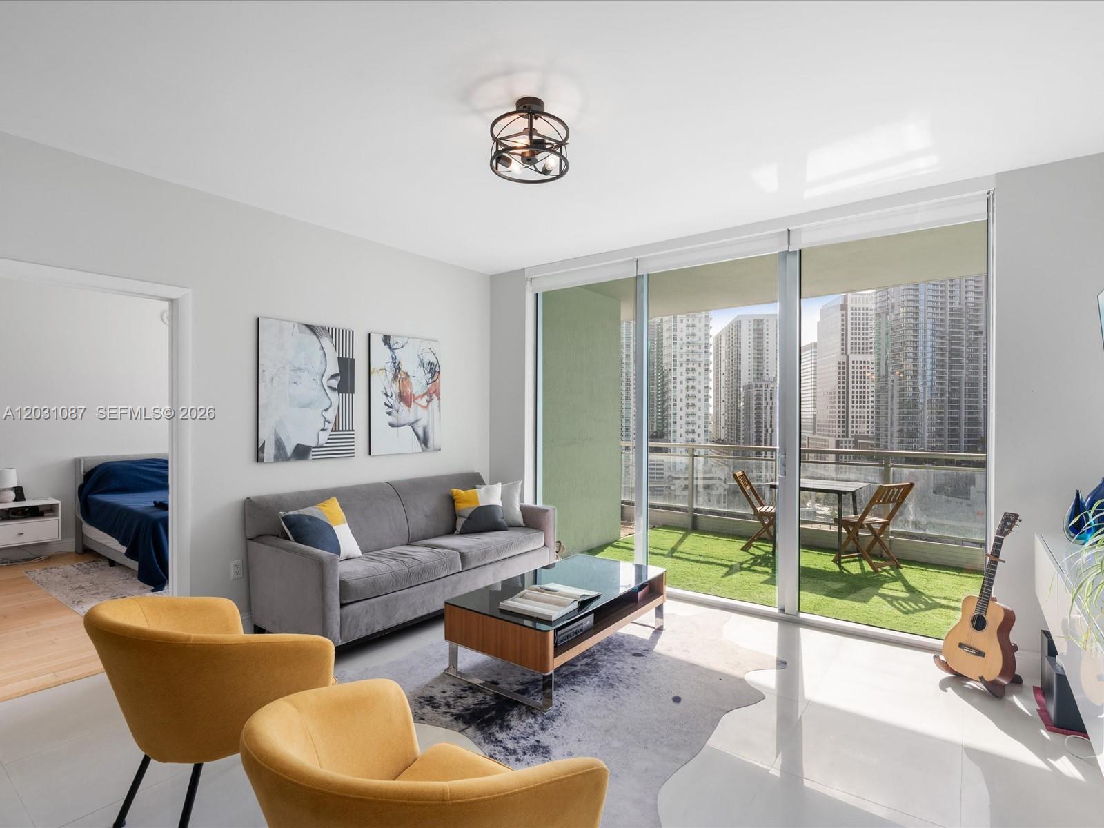 A living room features a gray sofa, yellow armchairs, and a balcony with city views — 90 SW 3rd St # 2015, Miami FL 33130, MIAMI, FL