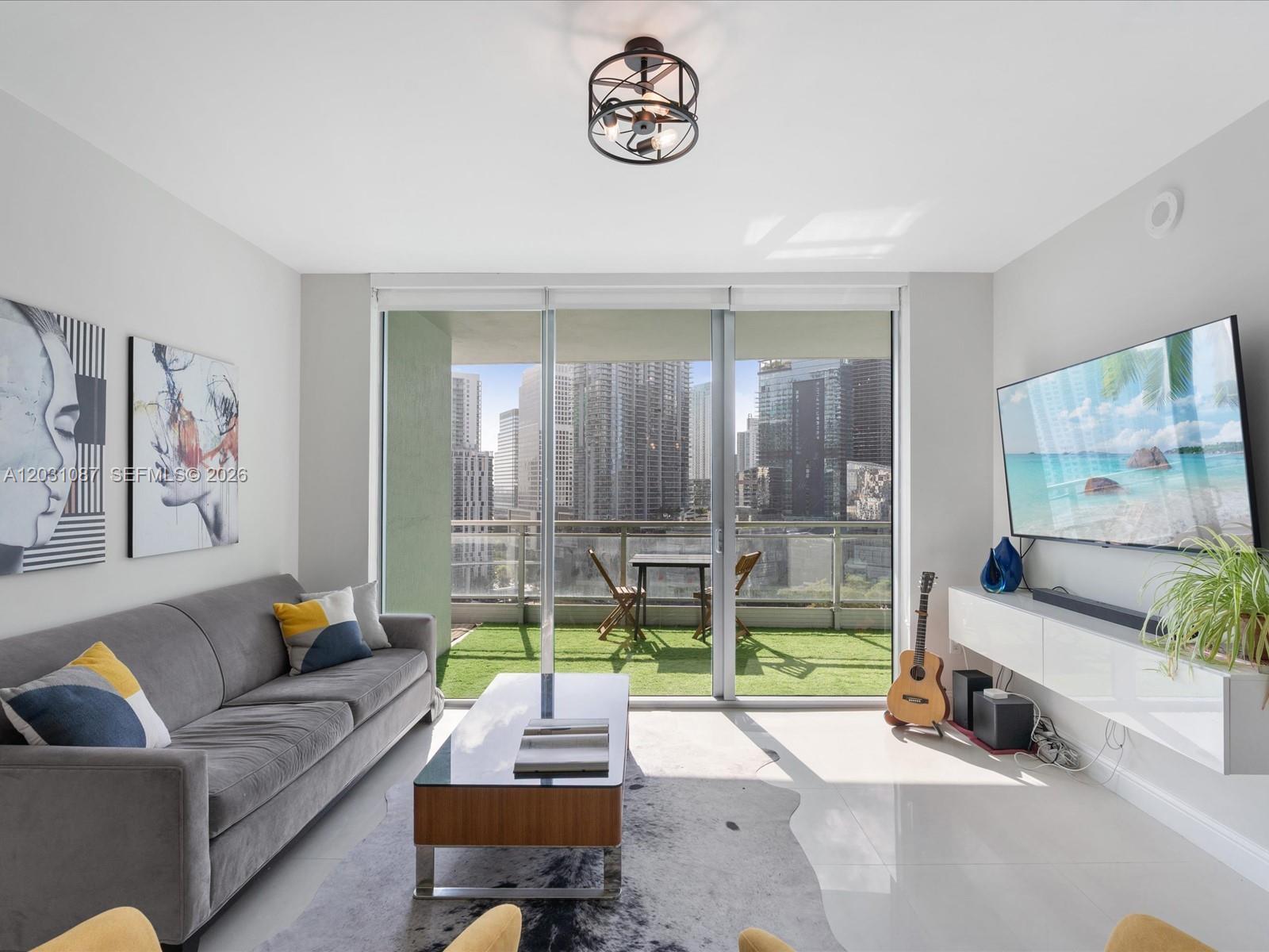A modern living room features a gray sofa, coffee table, and balcony with city views — 90 SW 3rd St # 2015, Miami FL 33130, MIAMI, FL