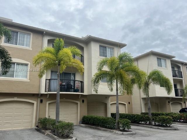 A multi-story residential building features beige stucco walls, balconies, and palm trees in front — ROYAL PALM BEACH, FL