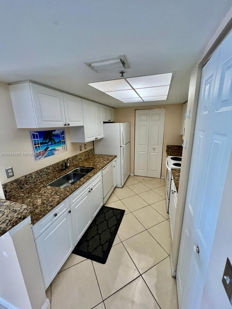 A kitchen features white cabinets, granite countertops, a stainless steel sink, and tile flooring — ROYAL PALM BEACH, FL