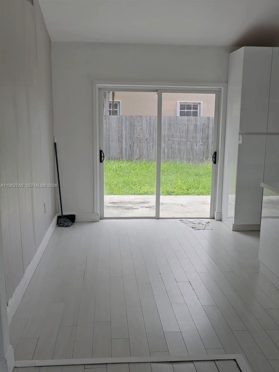 A room with white wood-look flooring and a sliding glass door leading to a backyard — PALMETTO BAY, FL