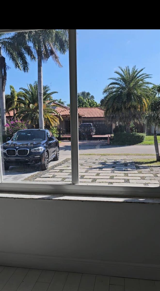 A view through a window shows a driveway, a parked car, and a neighboring house — PALMETTO BAY, FL