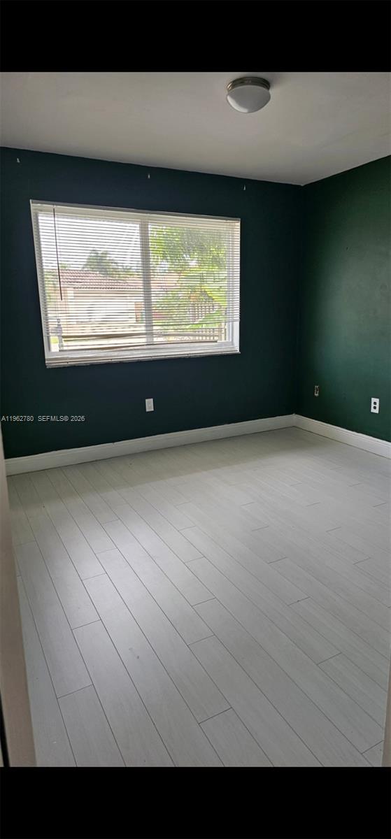 An empty bedroom features dark green walls, light wood-look flooring, and a window with blinds — PALMETTO BAY, FL
