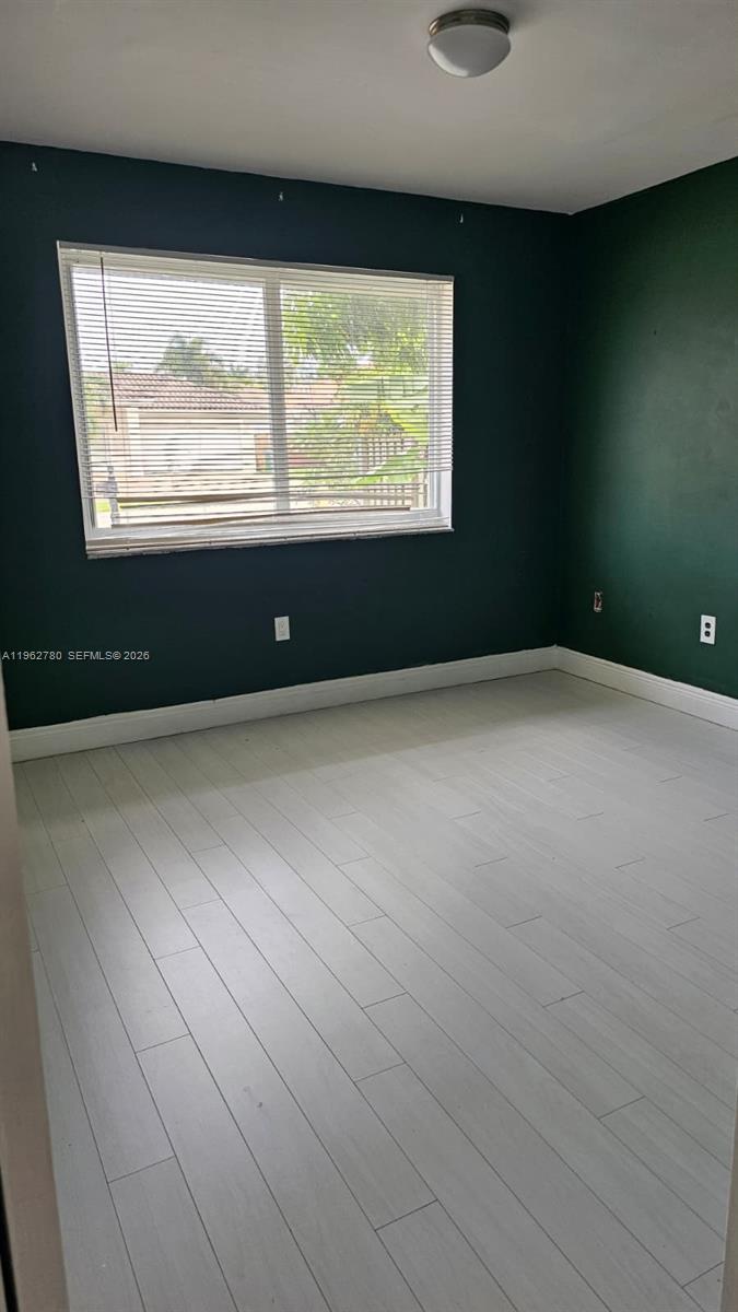 A bedroom features dark green walls, light wood-look flooring, and a window with blinds — PALMETTO BAY, FL