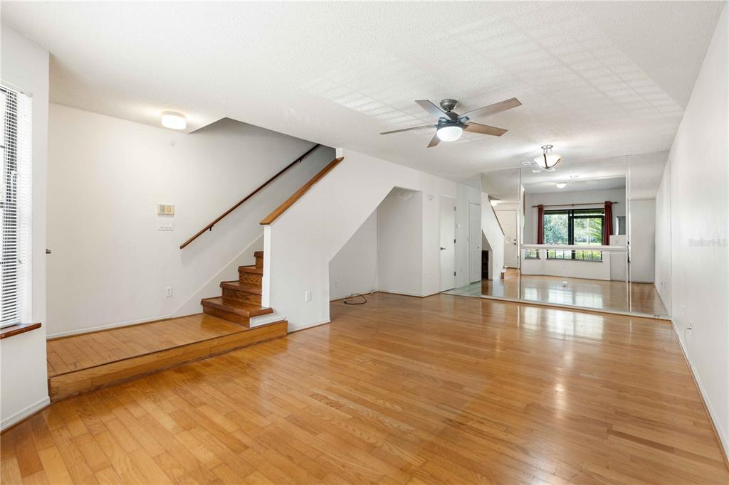 An empty living room features hardwood floors, a staircase with a wooden railing, and mirrors — 5100 BURCHETTE ROAD UNIT 404, TAMPA, FL