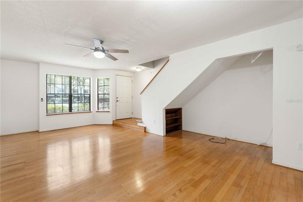 An empty living room features hardwood floors, a ceiling fan, and stairs with built-in shelving — 5100 BURCHETTE ROAD UNIT 404, TAMPA, FL