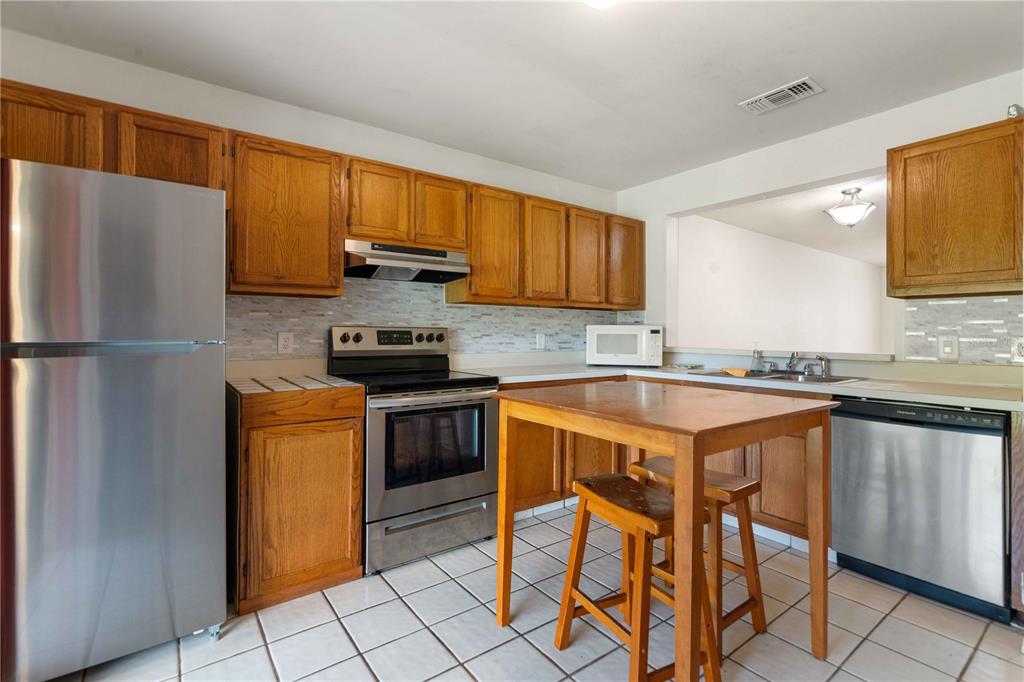 A kitchen features wood cabinets, stainless steel appliances, a tile backsplash, and a wooden island — 5100 BURCHETTE ROAD UNIT 404, TAMPA, FL
