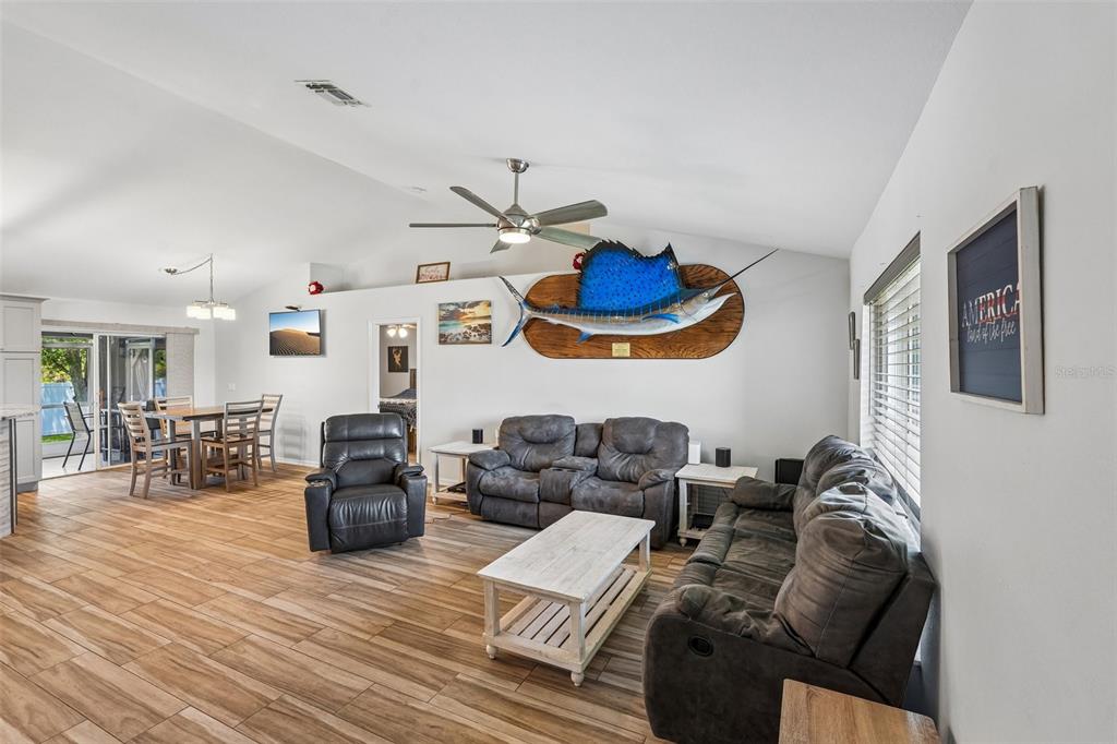 A living room with wood-look tile floors, a vaulted ceiling, and a mounted sailfish display — 4317 NW 40TH TERRACE, CAPE CORAL, FL