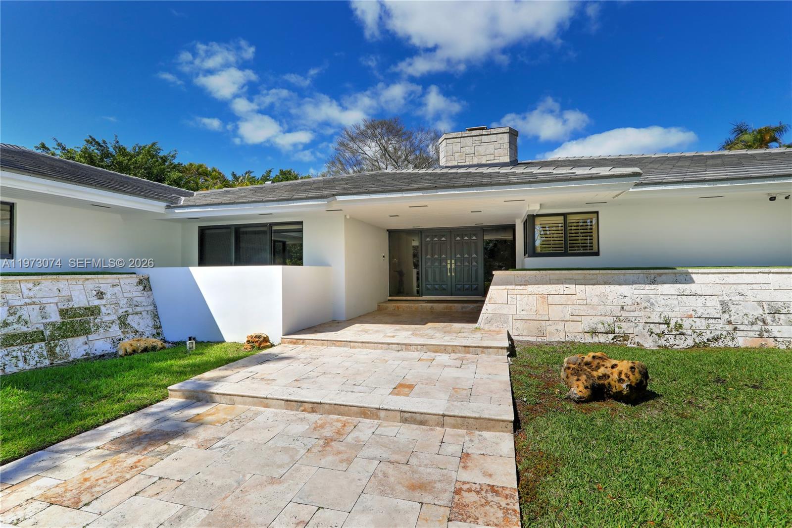 The exterior of a modern home features a stone walkway, white walls, and stone accents — 7322 Vistalmar St, Coral Gables FL 33143, CORAL GABLES, FL
