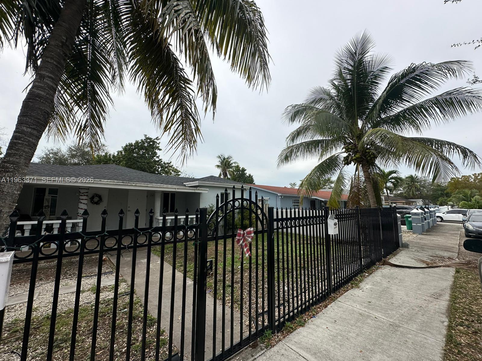 A black metal fence encloses the front yard of a single-story house with palm trees — 1128 NW 101st St, Miami FL 33150, MIAMI, FL