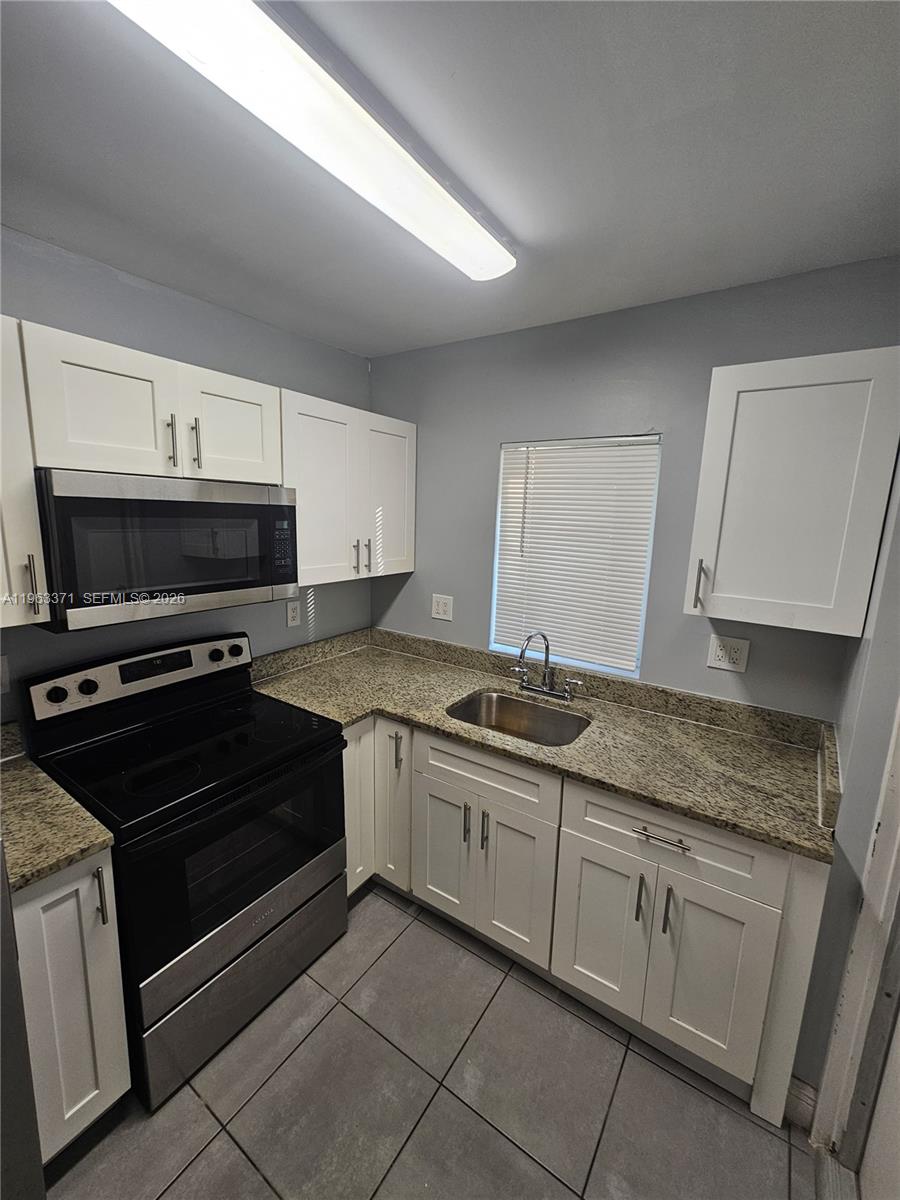 A kitchen features white cabinets, granite countertops, stainless steel appliances, and gray tile flooring — 1128 NW 101st St, Miami FL 33150, MIAMI, FL