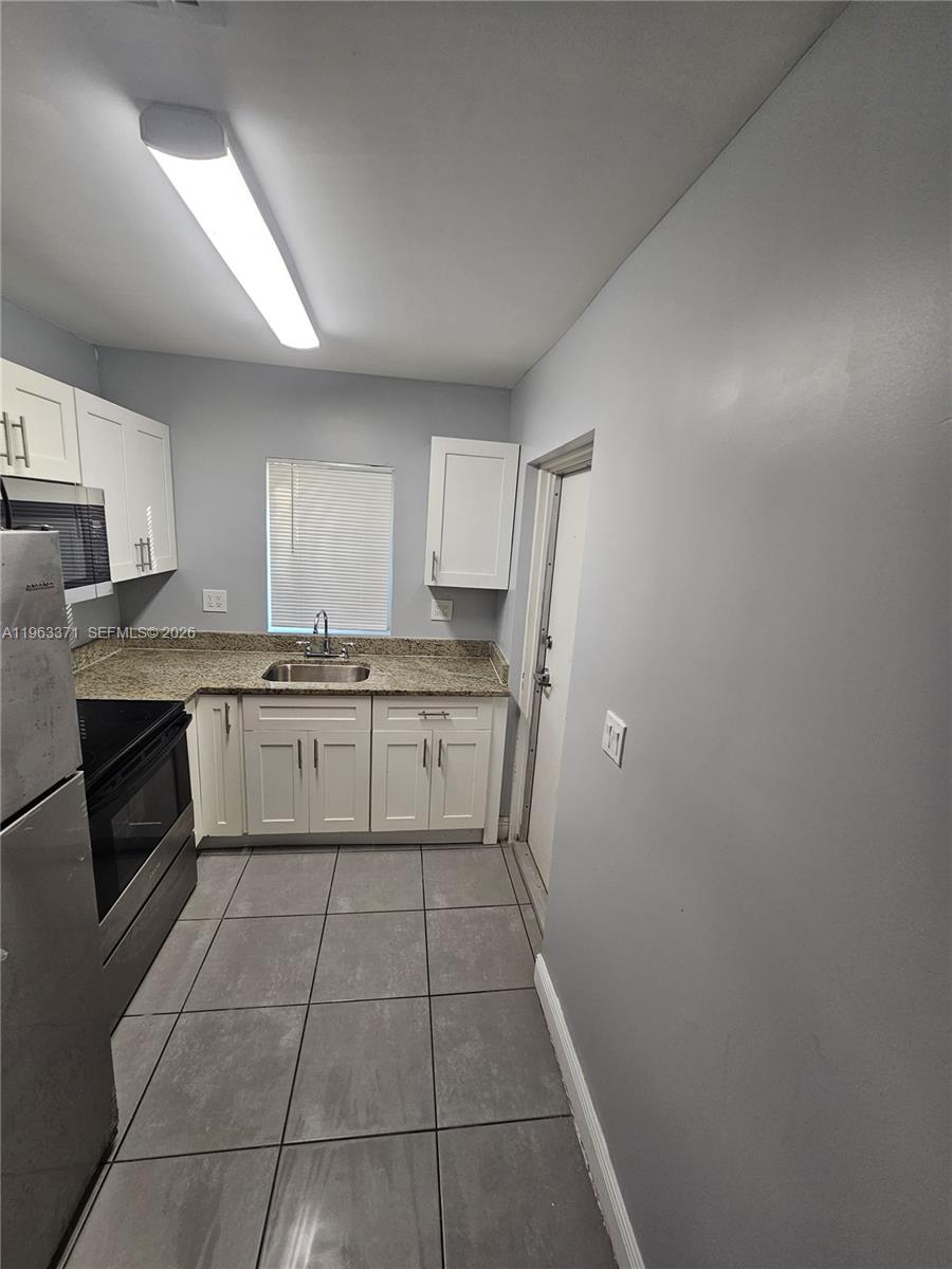 A kitchen features white cabinets, granite countertops, stainless steel appliances, and gray tile flooring — 1128 NW 101st St, Miami FL 33150, MIAMI, FL