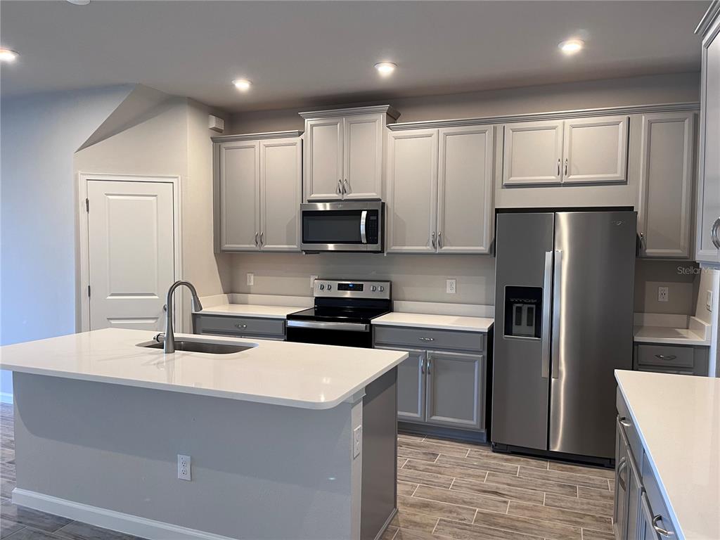 A kitchen features gray cabinets, white countertops, stainless steel appliances, and a central island — 2345 SUMMERLIT STREET, LUTZ, FL