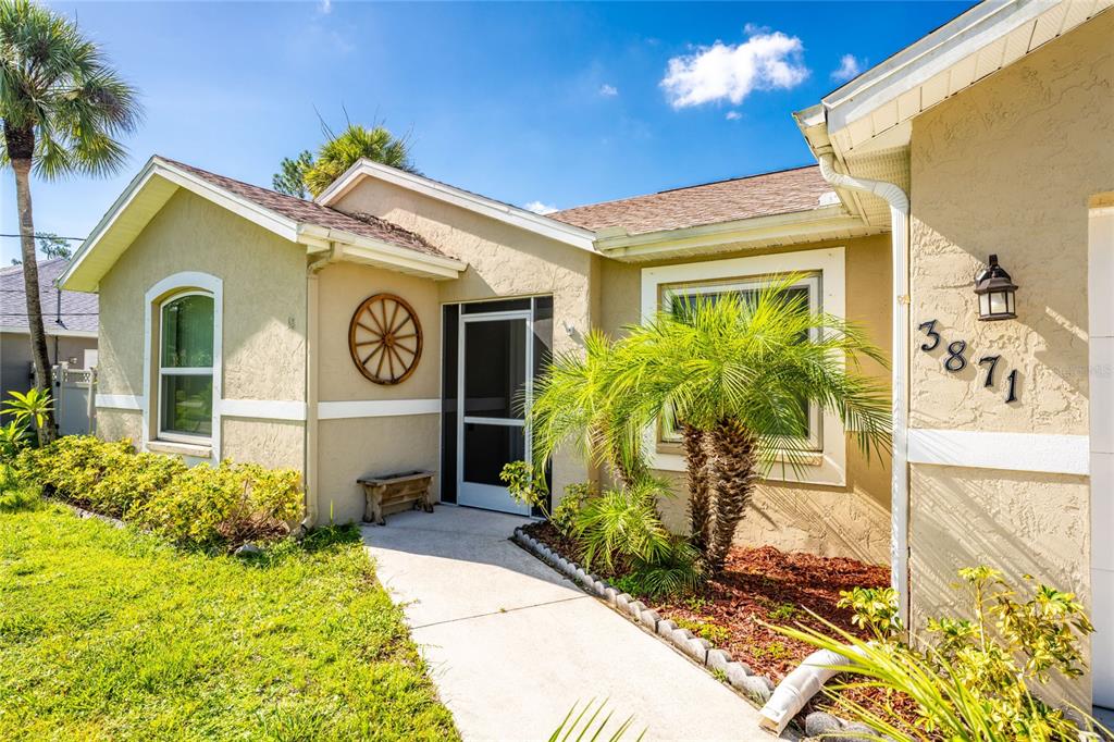 The exterior of a tan house features a front walkway, a palm tree, and a wagon-wheel decoration — 3871 COQUINA AVENUE, NORTH PORT, FL