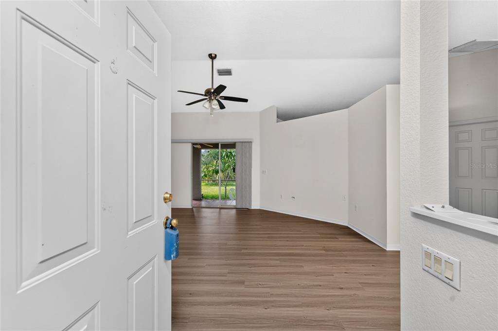 A view from an open doorway into a living area with wood-look flooring and sliding doors — 3871 COQUINA AVENUE, NORTH PORT, FL