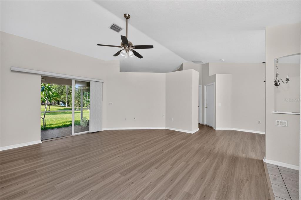 A spacious living room features light wood-look flooring, vaulted ceilings, a ceiling fan, and sliding doors — 3871 COQUINA AVENUE, NORTH PORT, FL