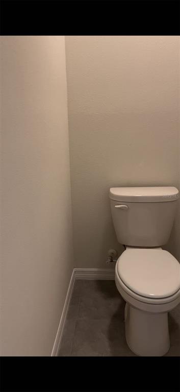 A white toilet is positioned in a small bathroom with light walls and gray flooring — 304 SOFIA LANE, LAKE ALFRED, FL