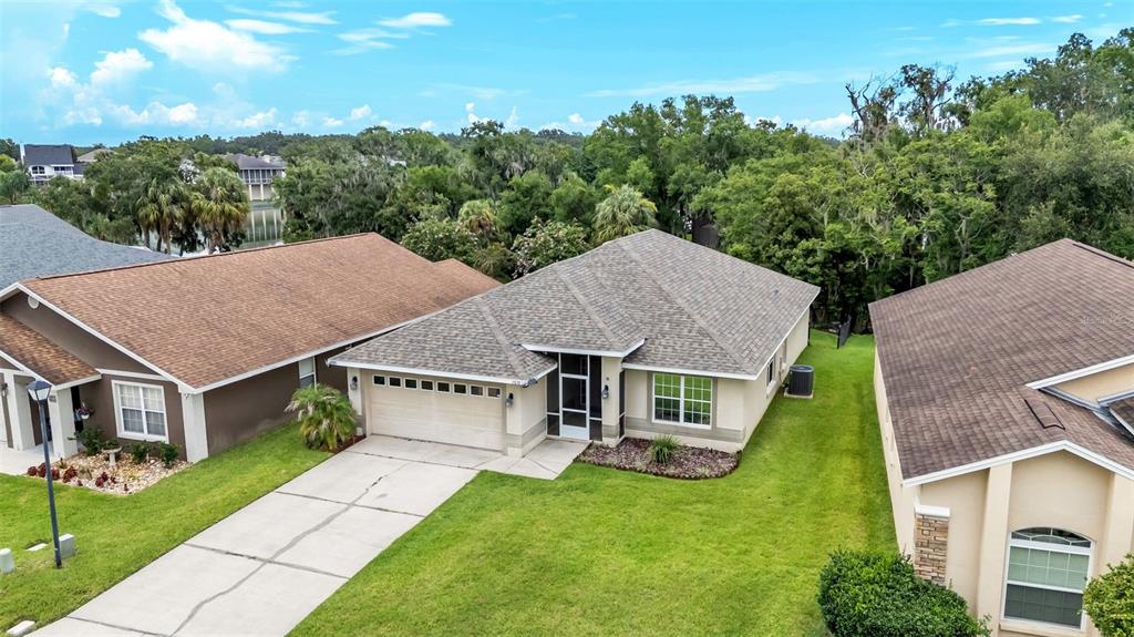 An aerial view shows a suburban house with a tan exterior, shingled roof, and driveway — 6838 SHIMMERING DRIVE, LAKELAND, FL