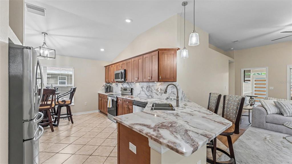 A kitchen with wood cabinets, marble-look countertops, and an island with bar seating — 6838 SHIMMERING DRIVE, LAKELAND, FL