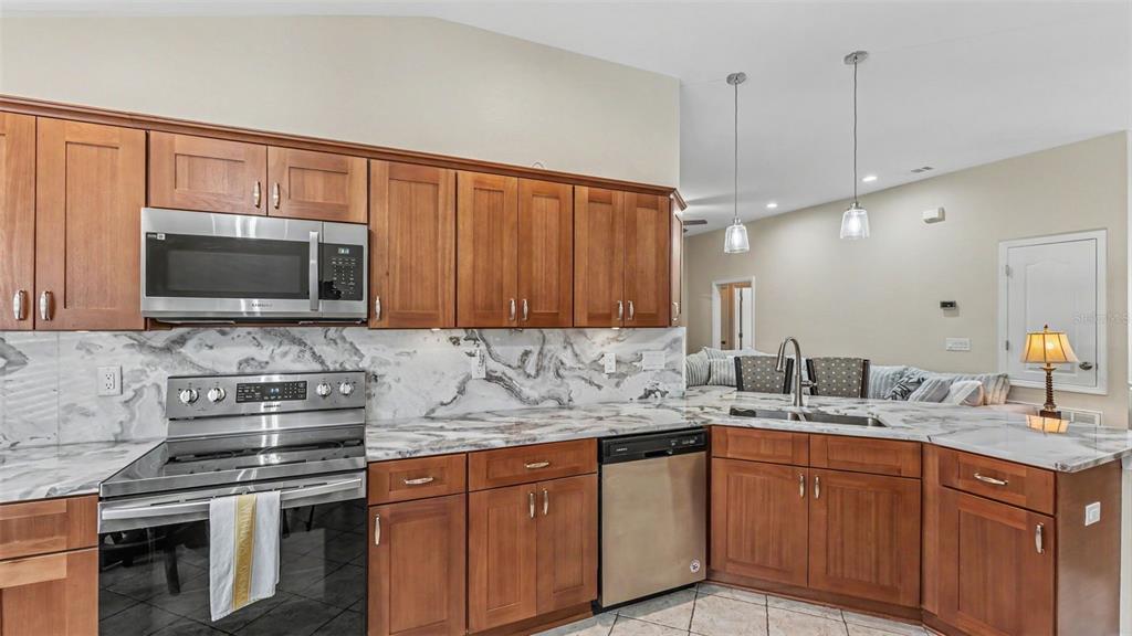 A kitchen features wood cabinets, stainless steel appliances, and marble-patterned countertops with a matching backsplash — 6838 SHIMMERING DRIVE, LAKELAND, FL