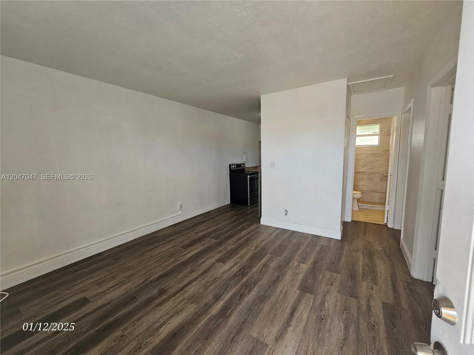 An interior view shows a living area with wood-look flooring, white walls, and a bathroom — 11752 SW 212th St # 0, Miami FL 33177, MIAMI, FL