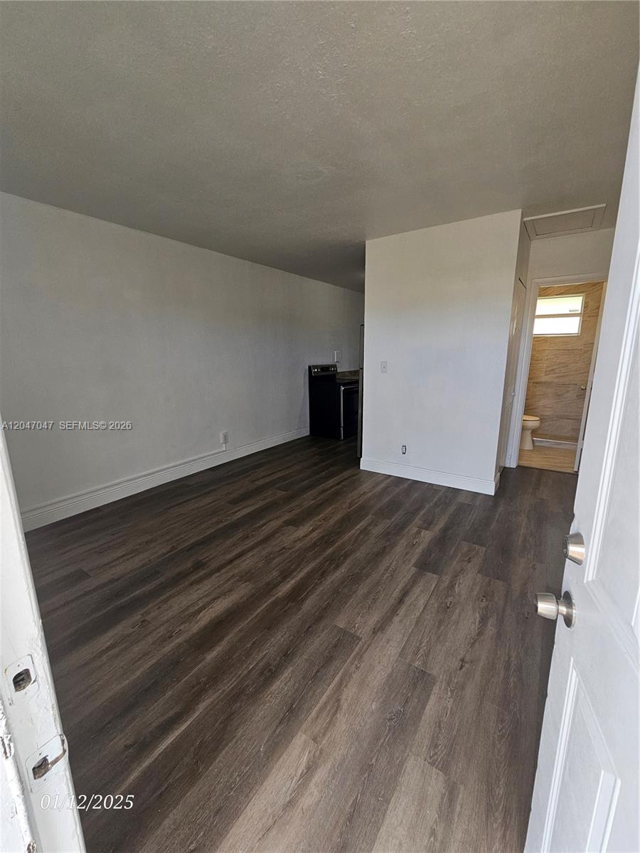 This room features dark wood-look flooring, white walls, and an adjacent bathroom and kitchen area — 11752 SW 212th St # 0, Miami FL 33177, MIAMI, FL