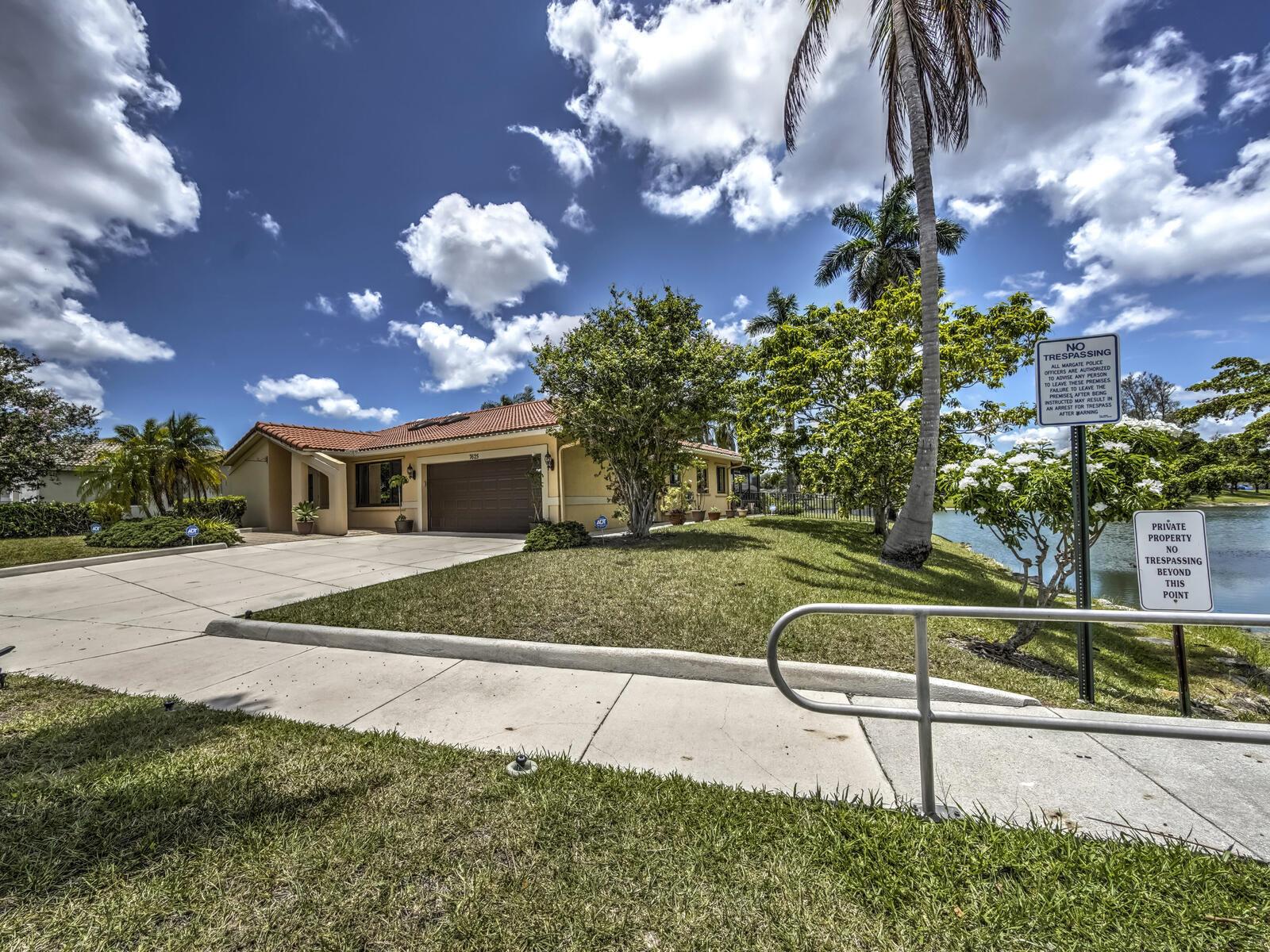 A single-story house with a tile roof and garage sits beside a lake — 7625 Sunflower Drive, Margate FL 33063, MARGATE, FL